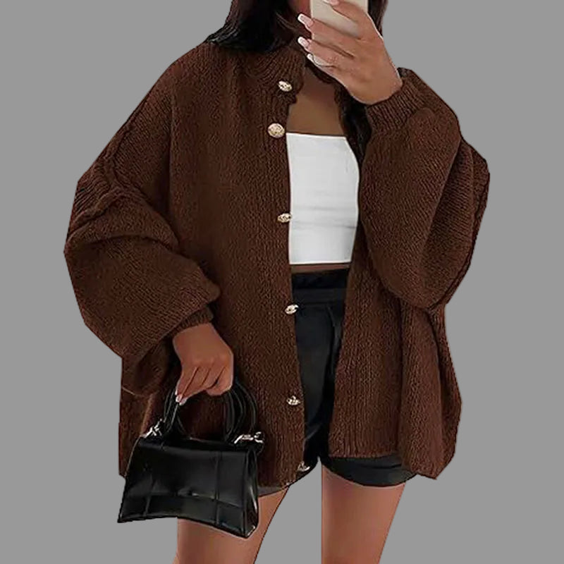 Person wearing a brown cardigan over a white top and black shorts, holding a phone and a black handbag.